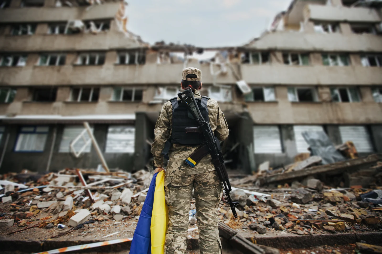 Guerre Ukraine 2026: 5 nouvelles menaces tuent le combat traditionnel. 1 Combattant ukrainien avec drapeau face à un bâtiment détruit