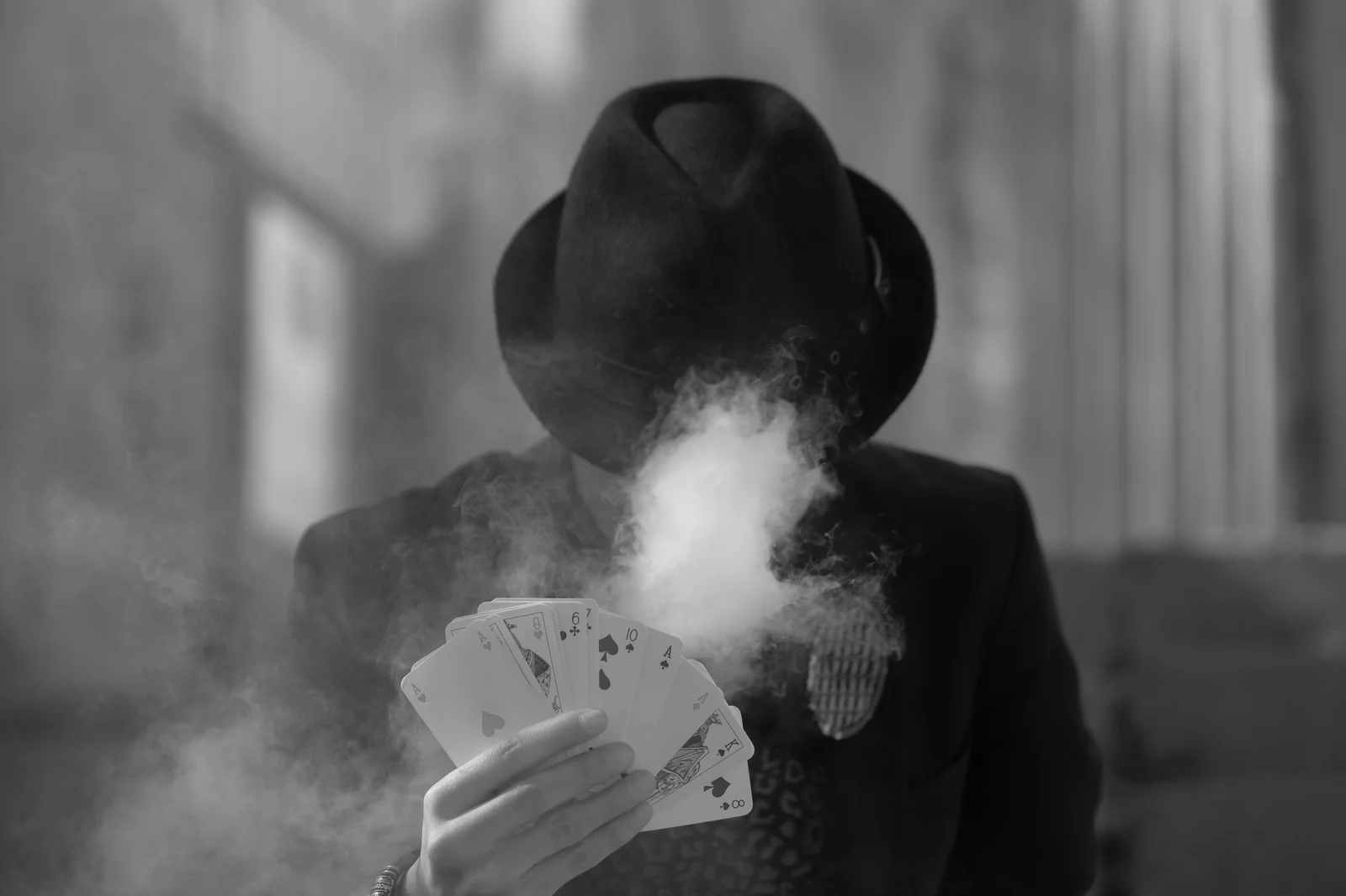 Silhouette mysterieuse au chapeau jouant les cartes dans la fumee, metaphore de l interview criminelle ou le predateur teste sa victime avant le passage a l acte