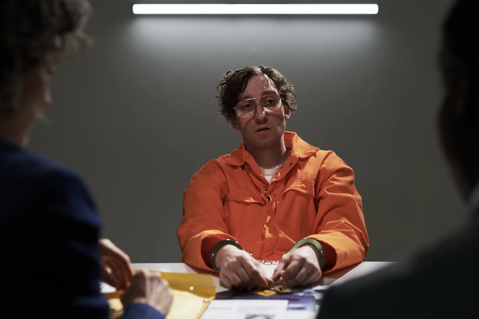 Detenu en combinaison orange face a des enqueteurs avec un regard insistant, illustration du target glance, premier signal pre-agression a reperer